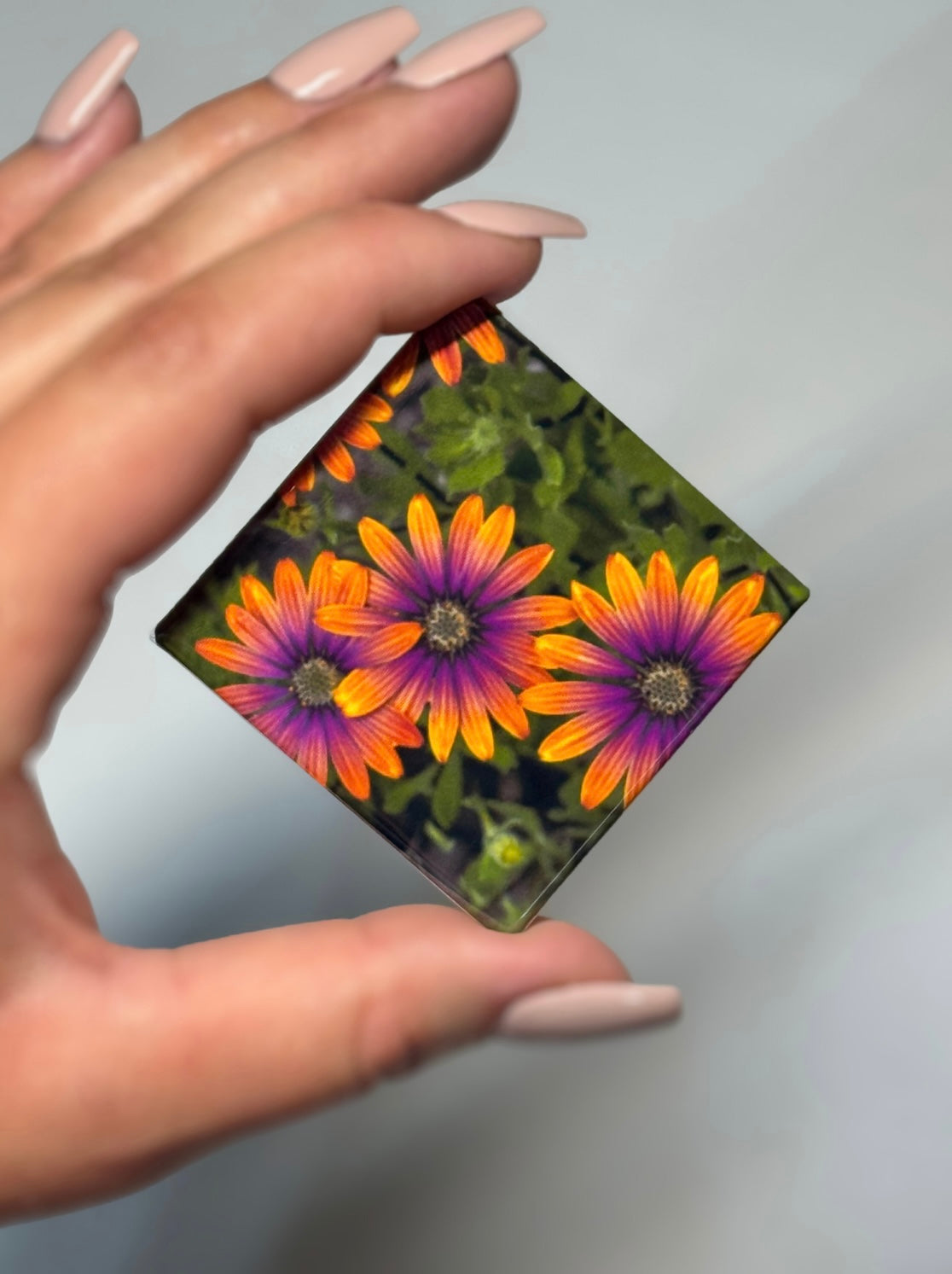 A square magnet with vibrant orange and pink flowers being held in a hand.