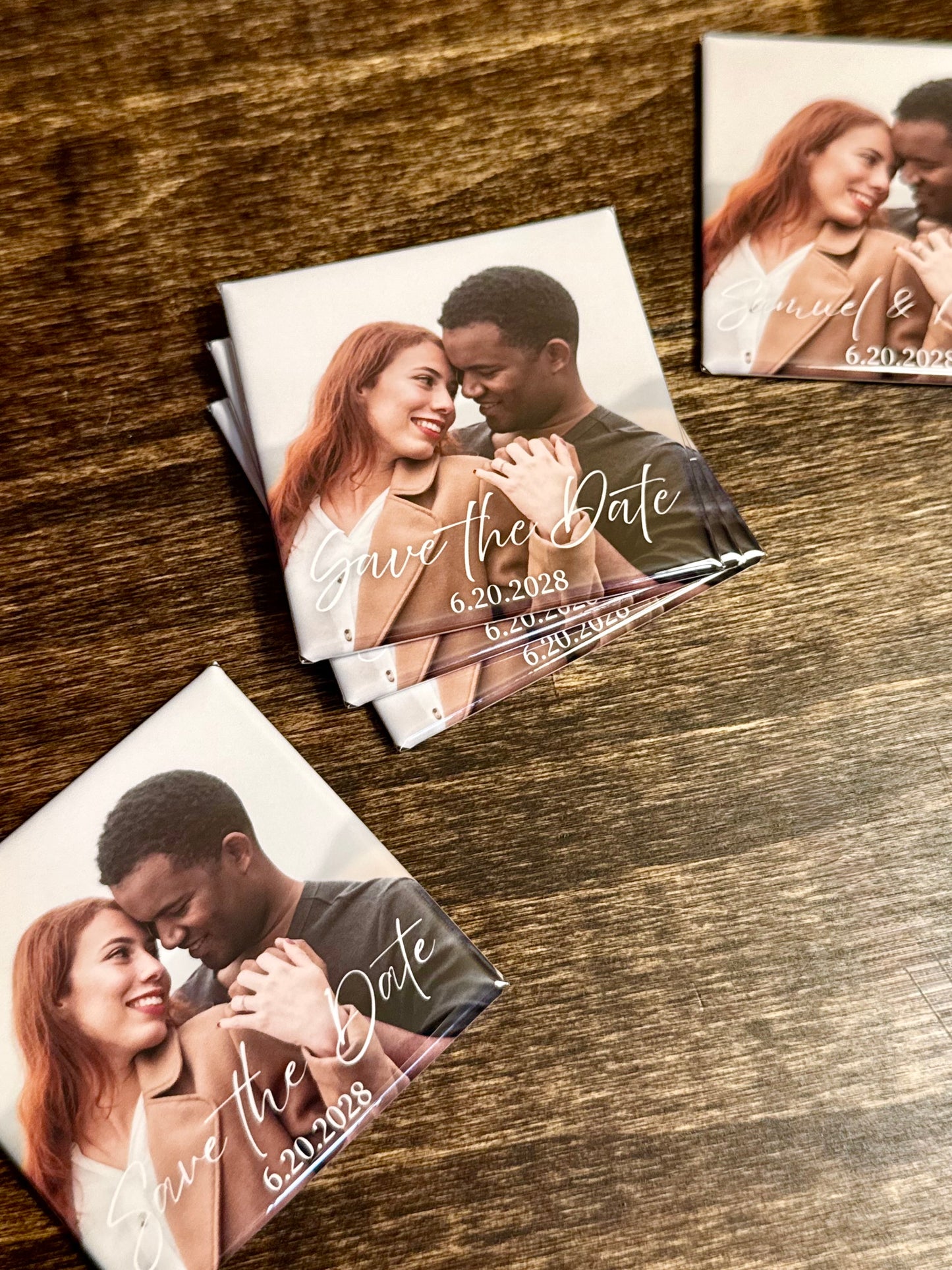 Collection of 2x2-inch custom photo magnets displayed on a wood table. "Save the date" is displayed on the magnets with a few different font options. 
