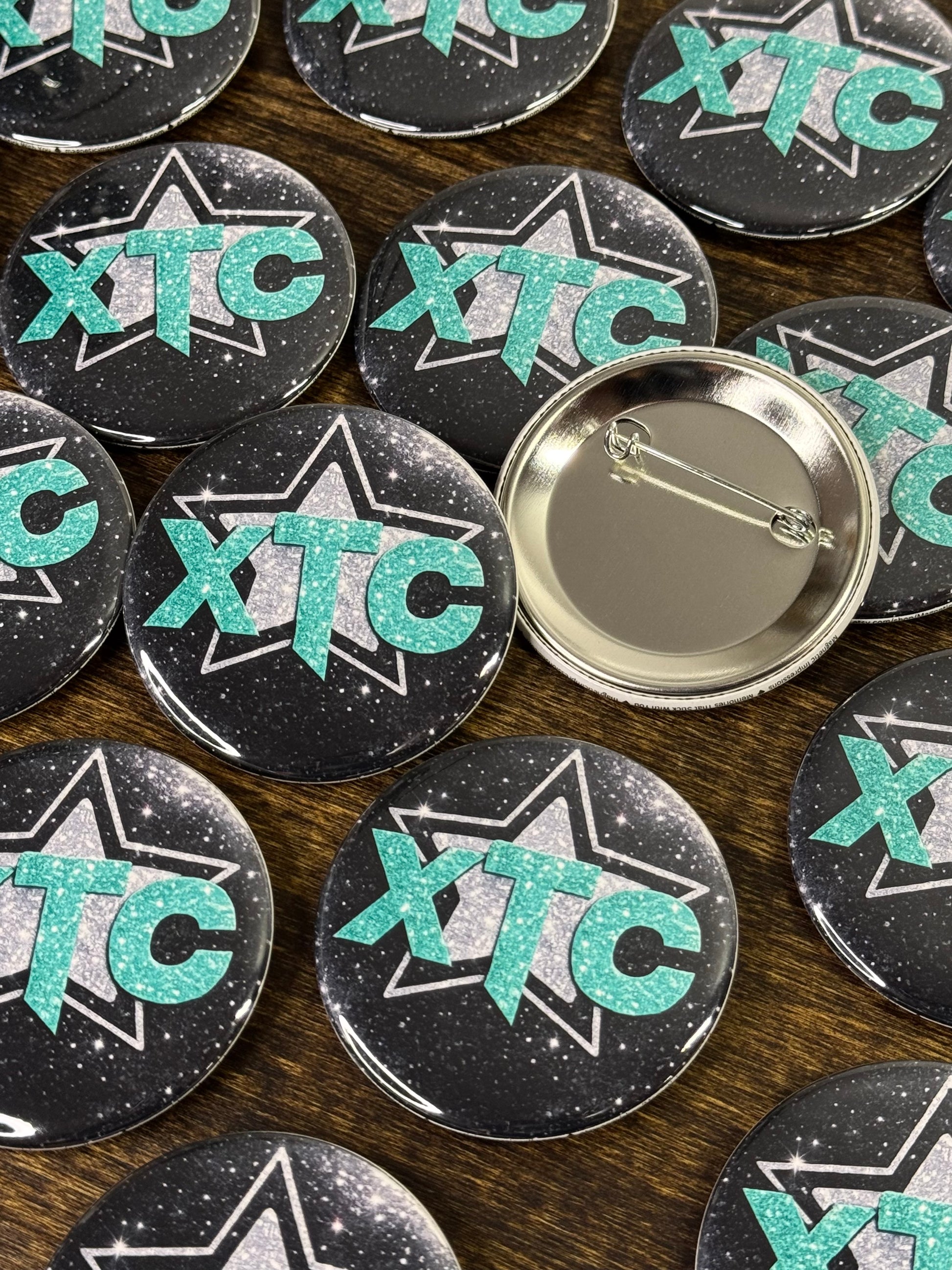 Collection of team buttons with the logo XTC on a wooden surface