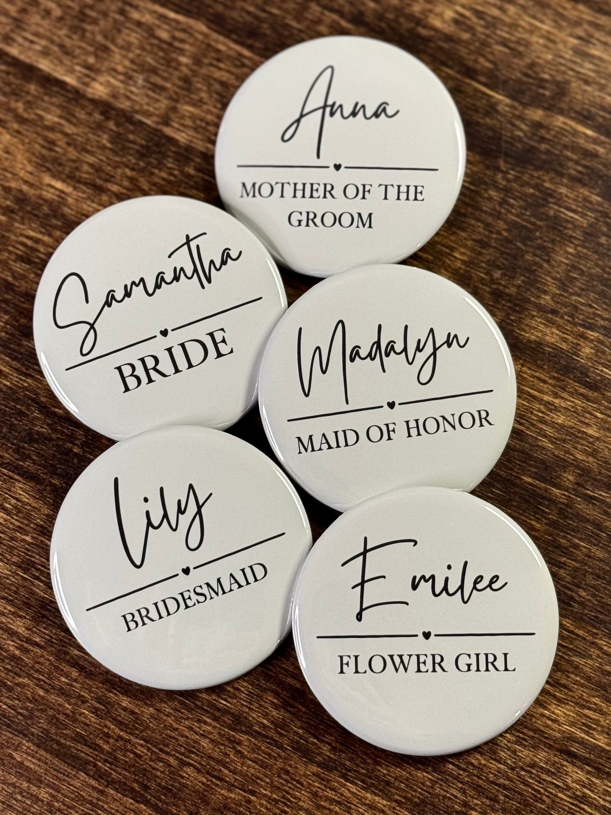 Set of light green pinback buttons with names and bridal party roles on a wooden surface